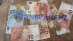 Geldscheine und Münzen hinter einer durchsichtigen Folie, auf der das Wort Transparenz geschrieben steht.