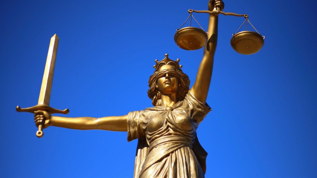 Goldene Justizia-Statue mit verbunden Augen vor blauem Himmel