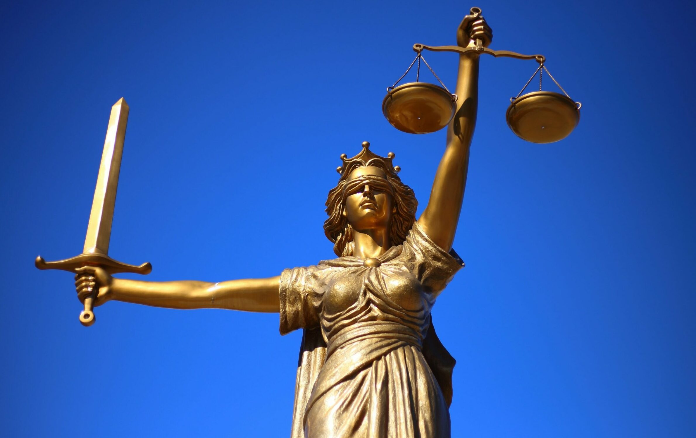 Goldene Justizia-Statue mit verbunden Augen vor blauem Himmel