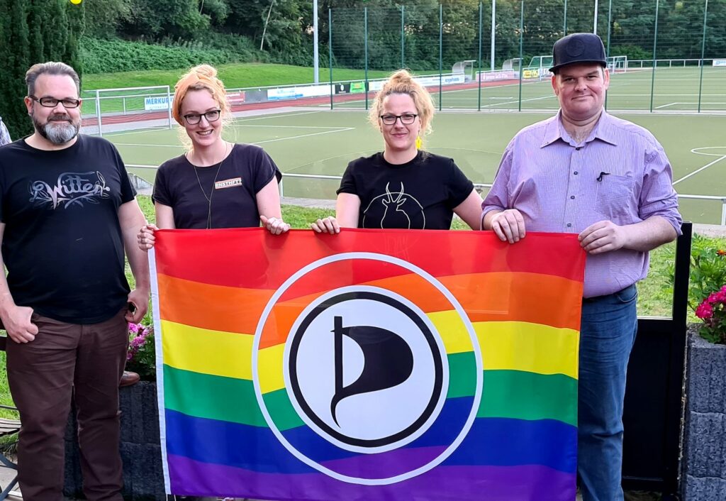 Elaine und Maria Bach, Patrick Bodden und Stefan Borggraefe halten zusammen eine Queeraten-Flagge