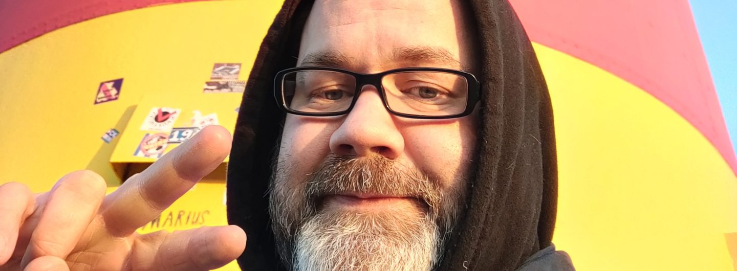 Stefan Borggraefe mit Hoodie vor einem Leuchtturm. Mit der rechten Hand macht er ein Victory-Zeichen.