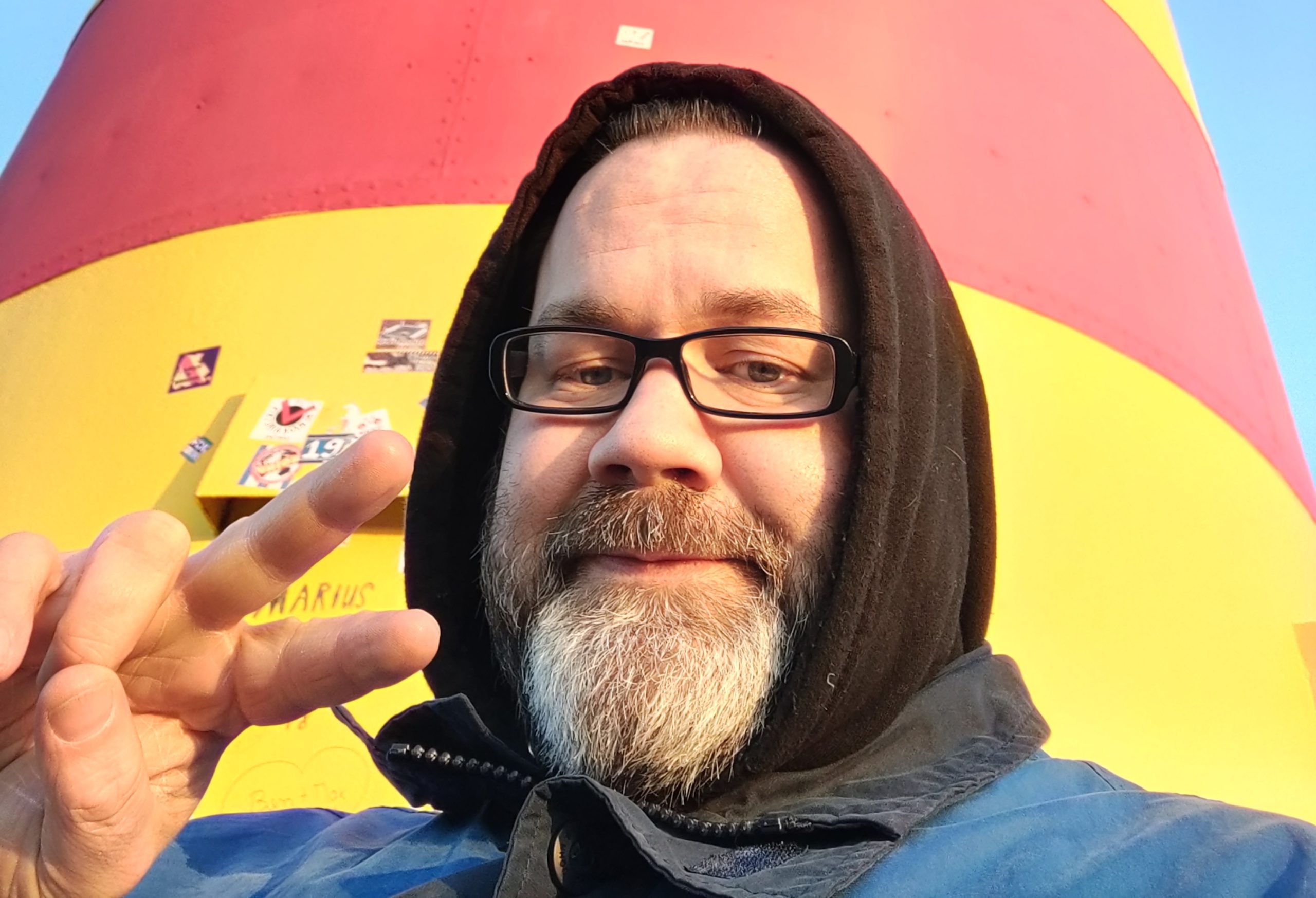 Stefan Borggraefe mit Hoodie vor einem Leuchtturm. Mit der rechten Hand macht er ein Victory-Zeichen.